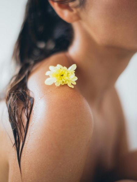 Close-up of a woman relaxing in a bath with a yellow flower on her shoulder.